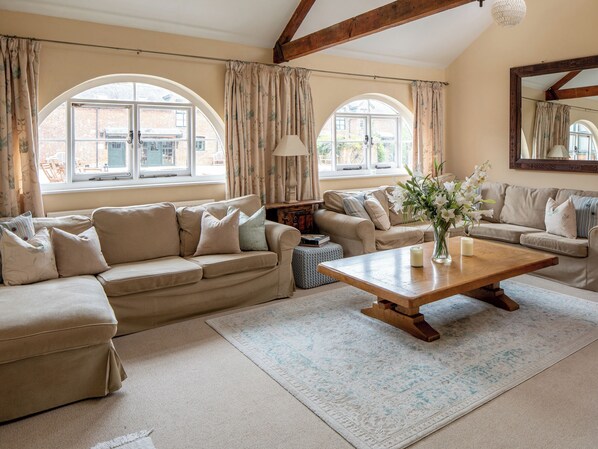 A spacious living room with a large sofa, a coffee table, and a view through arched windows.