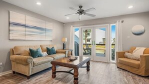 A living room with a sofa, coffee table, ceiling fan, and large windows. - Waterfront Getaway with private boat slip on desirable Key Allegro, Rockport Tx (Rockport)