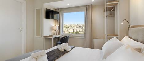 A hotel room with a bed, a desk, a chair, a TV, and a window with a city view.