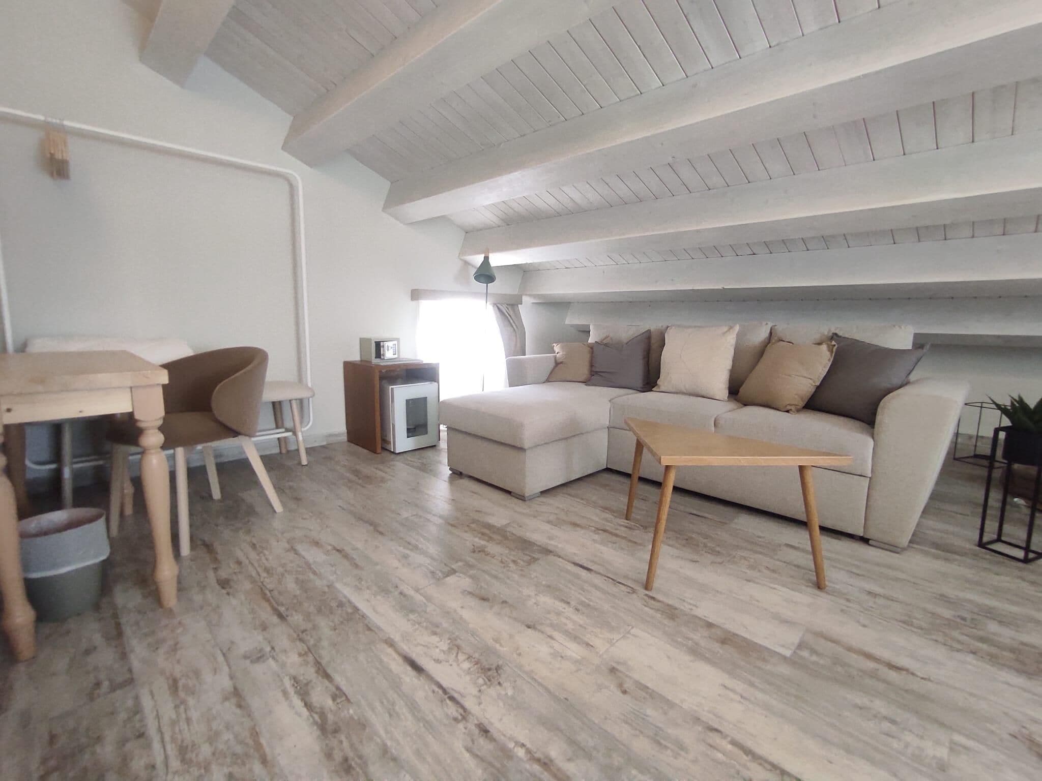 Ein modernes Wohnzimmer mit Holzboden, einer Couch, einem Couchtisch, einem kleinen Tisch und einer TV-Konsole.