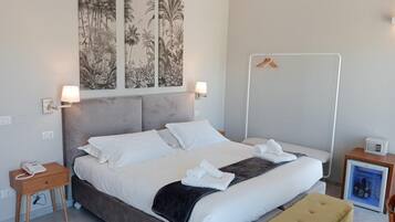 Une chambre d’hôtel moderne avec un grand lit, une table de chevet avec une lampe, une petite table de chevet avec un téléphone, un mini-bar et un porte-manteau mural.