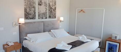 Una habitación de hotel moderna con una cama grande, una mesita de noche con lámpara, una pequeña mesita con teléfono, un minibar y un perchero.