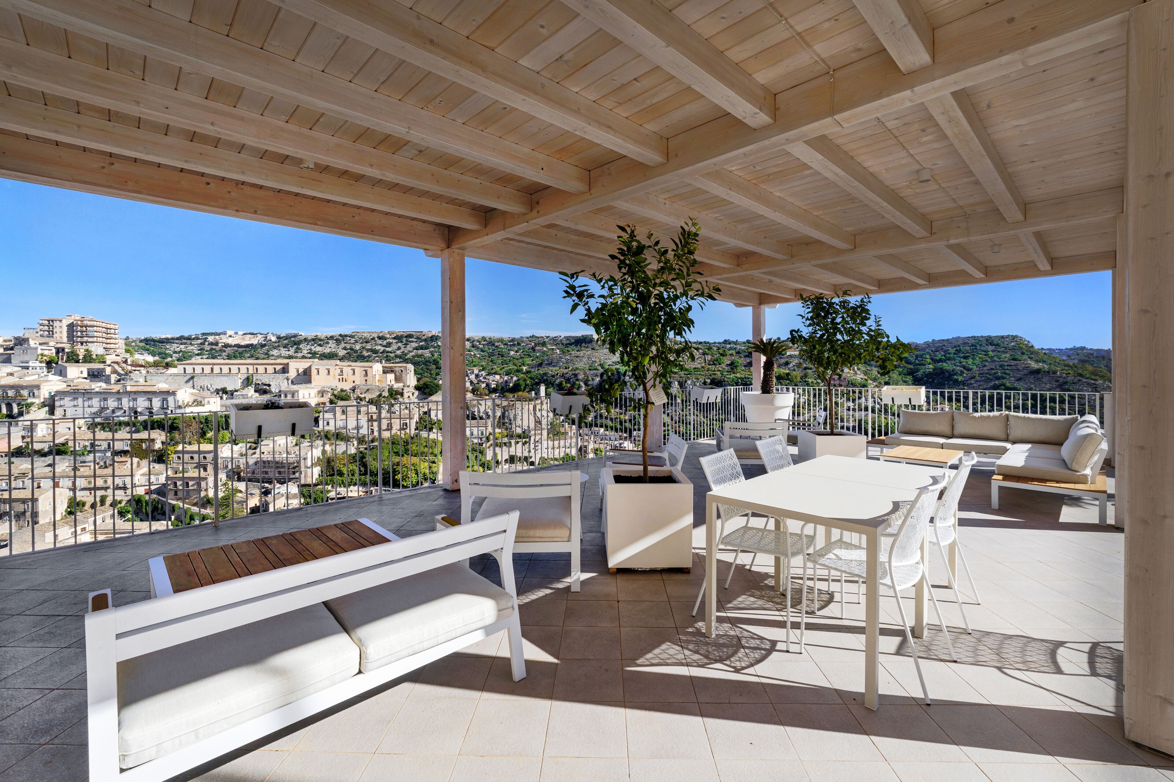 A covered outdoor seating area with white furniture, a table, and a potted plant.