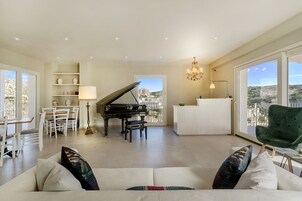 Een ruime woonkamer met een vleugelpiano, een witte bank en een groene fauteuil.