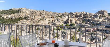 Ein Balkon mit gedecktem Frühstückstisch, mit Blick auf eine dicht bebauten Skyline.