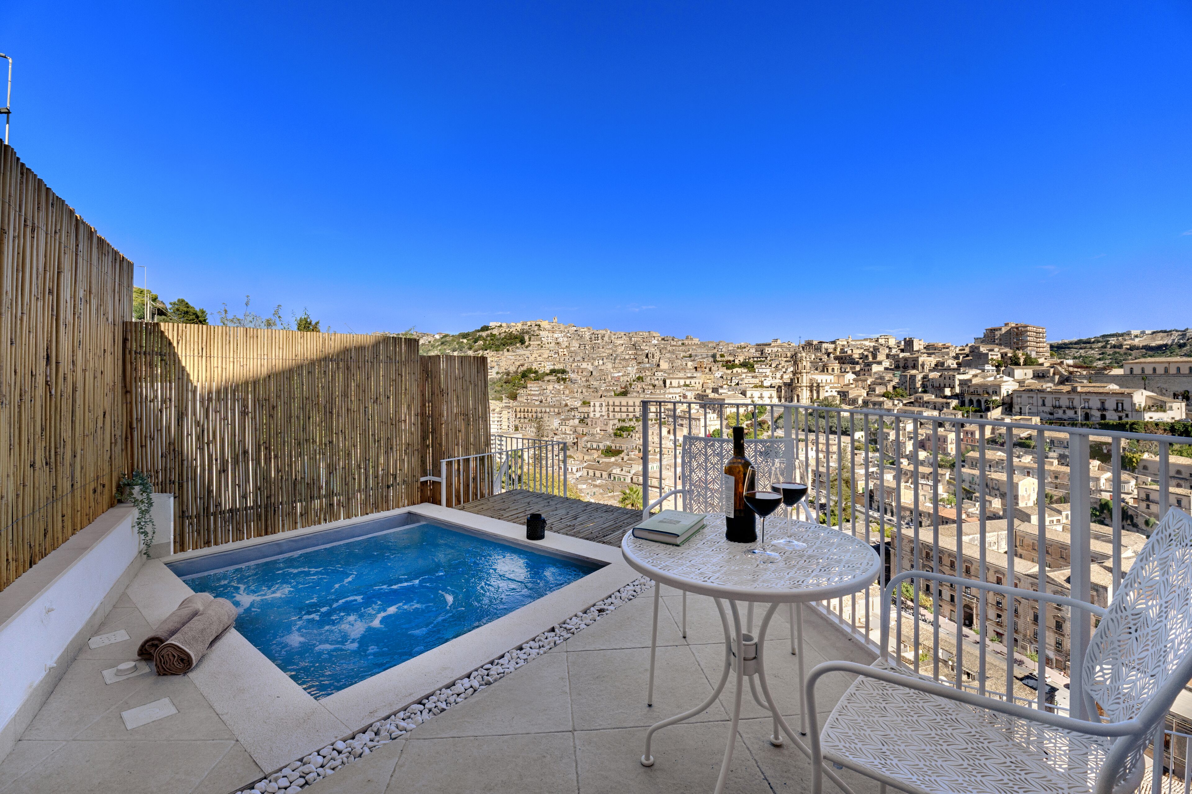 Eine Dachterrasse mit Pool, weißen Metallstühlen und einem Tisch mit Flasche und Gläsern.