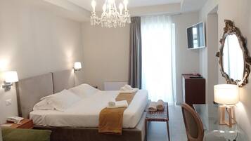 Habitación de hotel con una cama grande, un candelabro, un escritorio con lámpara, una silla y un espejo.