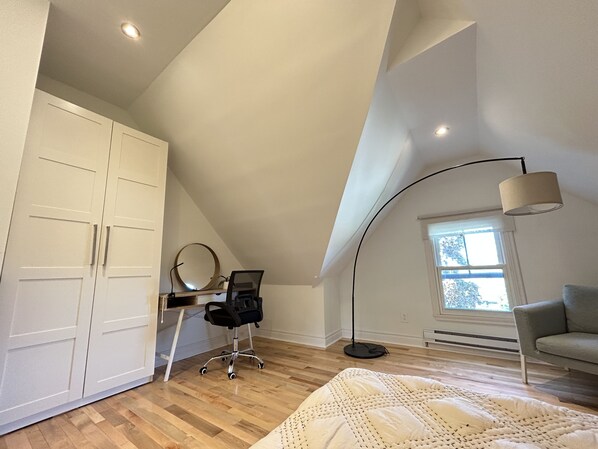 A bedroom with a sloped ceiling, a desk with a chair, a bed, a grey sofa, and a large window. - Cozy Attic Apartment in Grimsby (Grimsby)