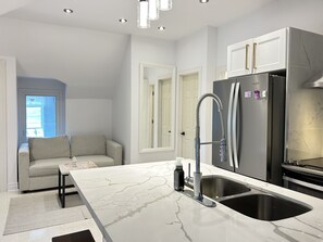 A modern kitchen with a marble countertop, stainless steel appliances, and a built-in sink. - Cozy Attic Apartment in Grimsby (Grimsby)