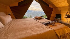 A cozy bedroom with a large bed, a view of the mountains, and a small table with a chair. - Cúspide Choachi Lodge (Choachí)