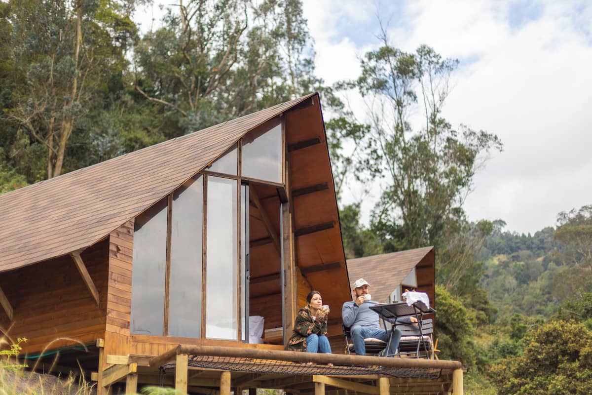 A wooden cabin with a large glass door, a deck, and a dining area.