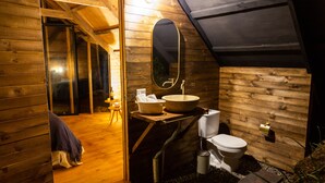 A compact, wooden interior with a large oval mirror, a sink, and a toilet. - Cúspide Choachi Lodge (Choachí)