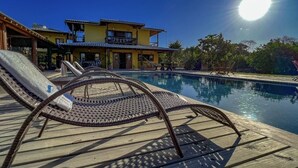 A pool area with lounge chairs and a building in the background. - Pousada Luz do Trevo (Porto Seguro)