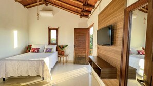 A bedroom with a bed, a TV, a wooden door, and a small table with a plant. - Pousada Luz do Trevo (Porto Seguro)