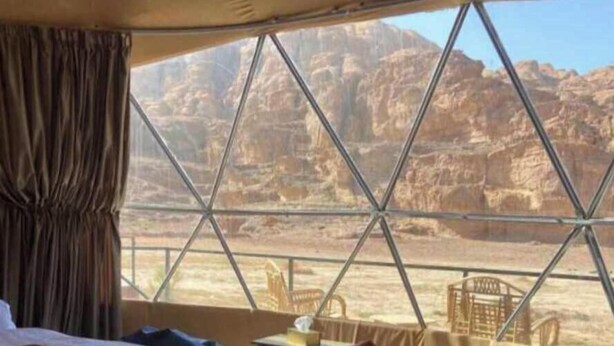 A room with a bed, a small table, and a window offering a view of rocky terrain. - Abdullah Ram  (Wadi Rum)