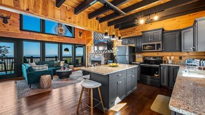 A spacious kitchen with dark cabinets, a large island, and a stone fireplace.