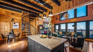 A spacious living area with a large island, a staircase, and a view through large windows.
