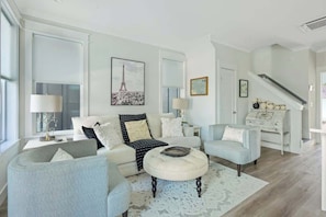 A modern living room with a sofa, armchairs, a coffee table, and a staircase.