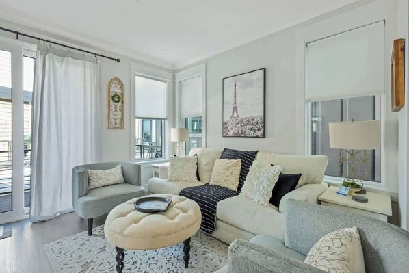 A living room with a sofa, ottoman, and a painting of the Eiffel Tower.