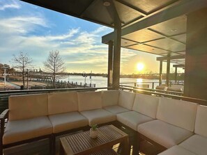A covered outdoor seating area with a view of a body of water and a sunset.