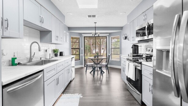 A modern kitchen with white cabinets, stainless steel appliances, and a dining area with a round table and chairs. - Leafy Lodge, Near Springs, Beach, Hot Tub, Fenced (Spring Hill)