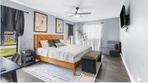 A modern bedroom with a wooden bed, a ceiling fan, a TV mounted on the wall, and a view of the outdoors. - Leafy Lodge, Near Springs, Beach, Hot Tub, Fenced (Spring Hill)