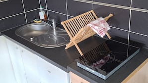 Una cocina con un lavabo, un tendedero de madera y una estufa negra.