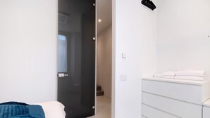 Een slaapkamer met een bed, een witte kapstok en een glazen deur die naar een hal leidt.