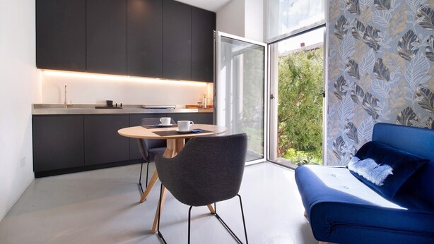 Een moderne keuken met donkere kasten, een eettafel met stoelen en een blauwe bank met kussen.