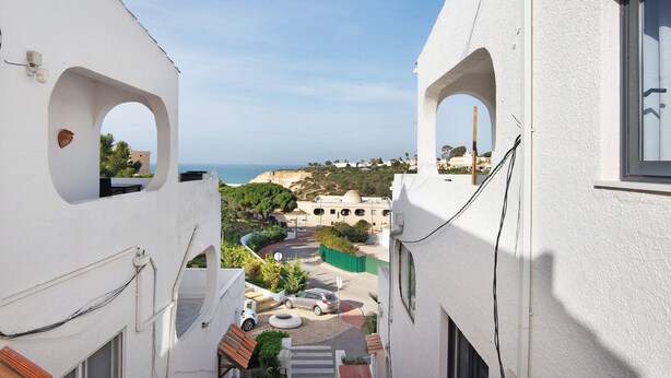 Una calle estrecha con edificios blancos, un coche y vista al mar.