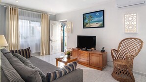 Una sala de estar con un sofá, televisión, sillón de mimbre y un cuadro de una playa.