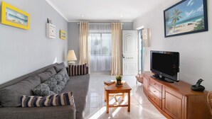 Una sala de estar con sofá, televisión, mueble de madera y puerta que da a un balcón.