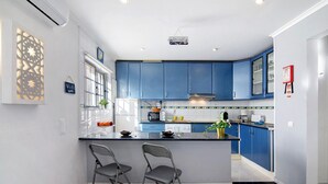 Una cocina moderna con armarios azules, una isla central con dos sillas, un microondas y una cafetera.