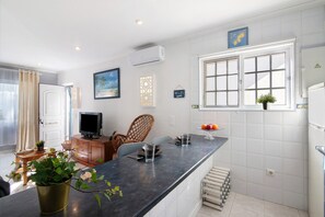 A modern kitchen with a black countertop, white tiled walls, a window with blinds, a television, and a potted plant. - Apartment 'Lemons' with Private Terrace, Wi-Fi and Air Conditioning (Carvoeiro)