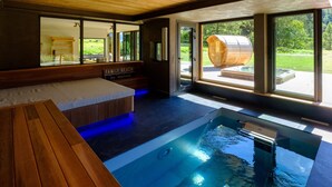A modern indoor pool with a wooden bench, large windows, and a view of a wooden barrel. - Chalet 'Aikoa' with Mountain View, Private Terrace and Wi-Fi (Chamonix-Mont-Blanc)