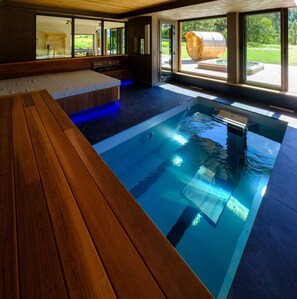 A modern indoor pool with a wooden bench, large windows, and a view of a wooden barrel. - Chalet 'Aikoa' with Mountain View, Private Terrace and Wi-Fi (Chamonix-Mont-Blanc)
