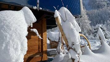 Una baita di legno con rami imbiancati dalla neve e un cielo azzurro intenso.