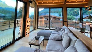 A modern interior with a large sofa, wooden beams, and large windows offering mountain views. - Chalet 'Aikoa' with Mountain View, Private Terrace and Wi-Fi (Chamonix-Mont-Blanc)