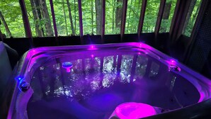 A hot tub with purple lighting, surrounded by a wooden deck and a view of a forest. - Romantic Fall Foliage Couples Escape | Hot Tub, EV Charger, 600 Mbps (Mars Hill)