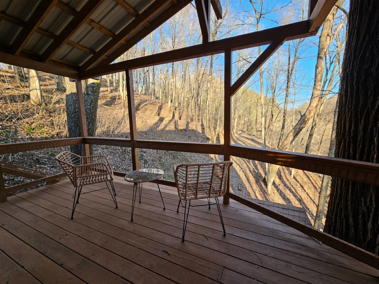 A wooden deck with two wicker chairs and a small table, overlooking a forested area.