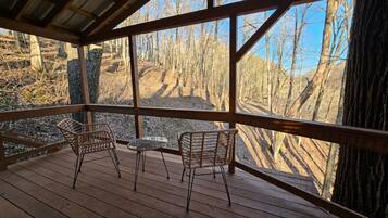 A wooden deck with two wicker chairs and a small table, overlooking a forested area.