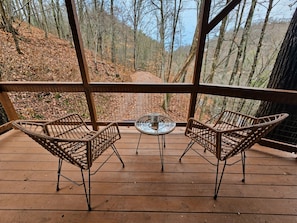 A wooden deck with wicker chairs and a small table, overlooking a forested area. - Romantic Fall Foliage Couples Escape | Hot Tub, EV Charger, 600 Mbps (Mars Hill)