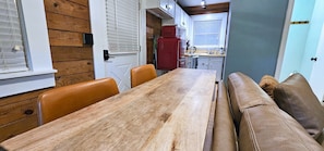 Un coin repas avec une table en bois et des chaises en cuir, une cuisine en arrière-plan et une porte bleue.