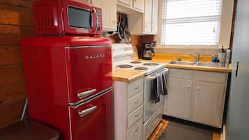 A compact kitchen with a red Galanz microwave, white cabinets, a wooden countertop, and a window with blinds.