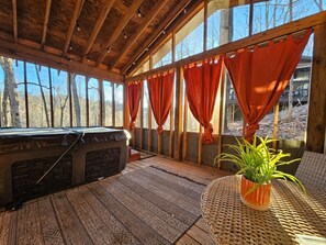 Una habitación acogedora con techo de vigas de madera, ventanas amplias con cortinas naranjas, un calentador portátil y una mesa de ratán trenzado con una planta en maceta.