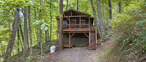 A wooden cabin with a balcony, surrounded by forest.