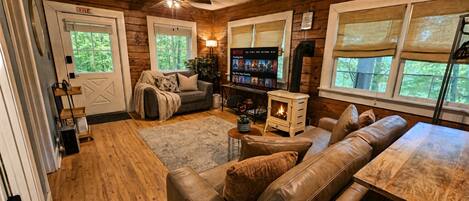 Cozy cabin living room with fireplace, big TV, and woodland views
