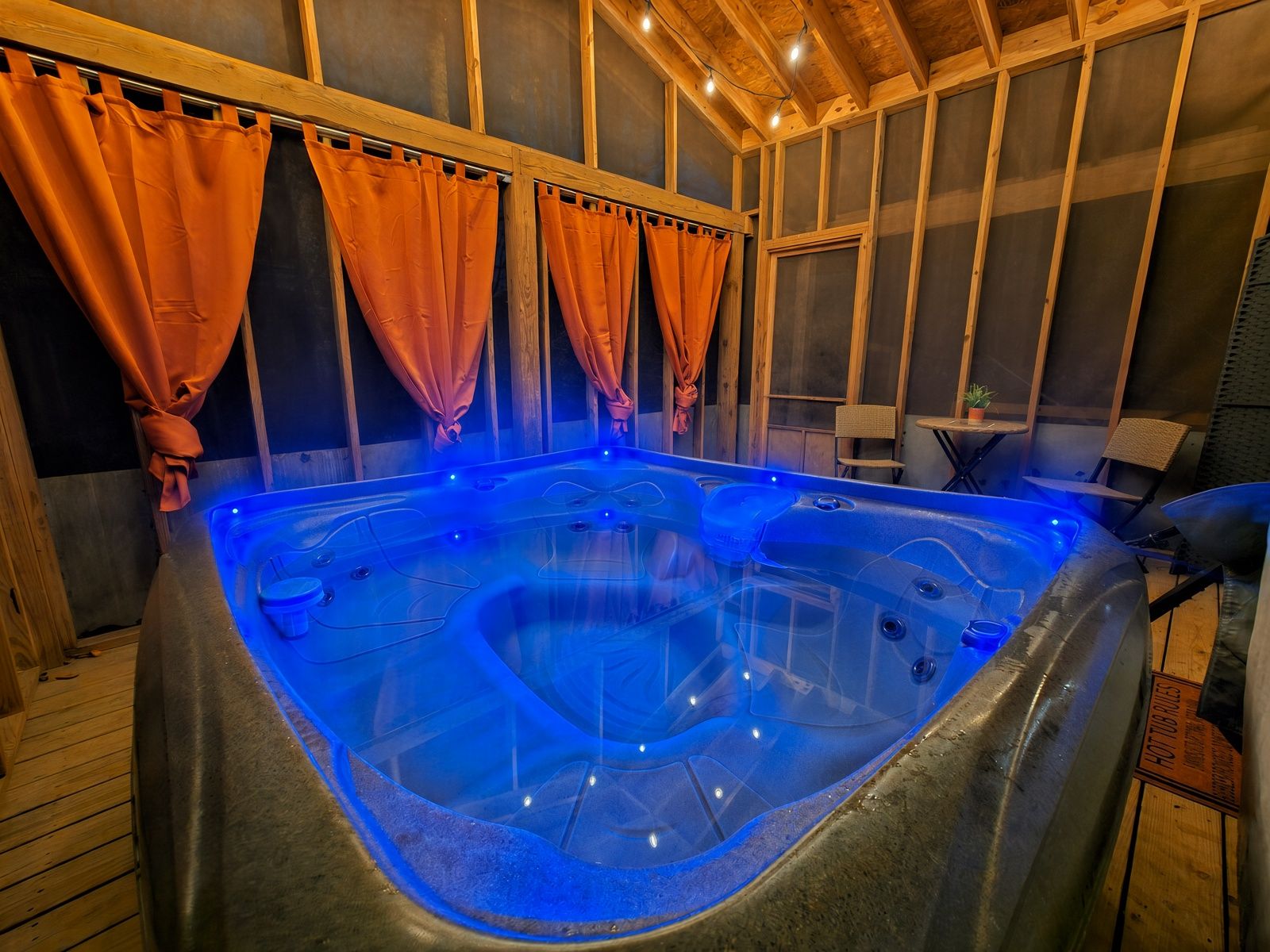 A hot tub with blue lighting, wooden walls, and orange curtains.
