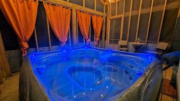 A hot tub with blue lighting, wooden walls, and orange curtains.