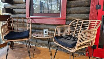 A log cabin with two wicker chairs and a small table with a mug.